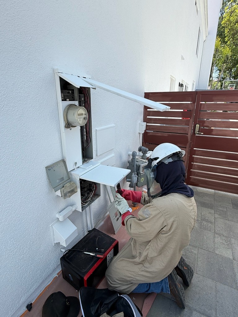 Technician in insulated gloves and face shield working on an exterior electrical service