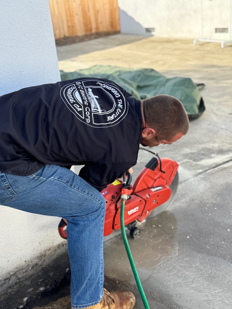 Electrical crew cutting concrete for conduit run during EV charger installation prep