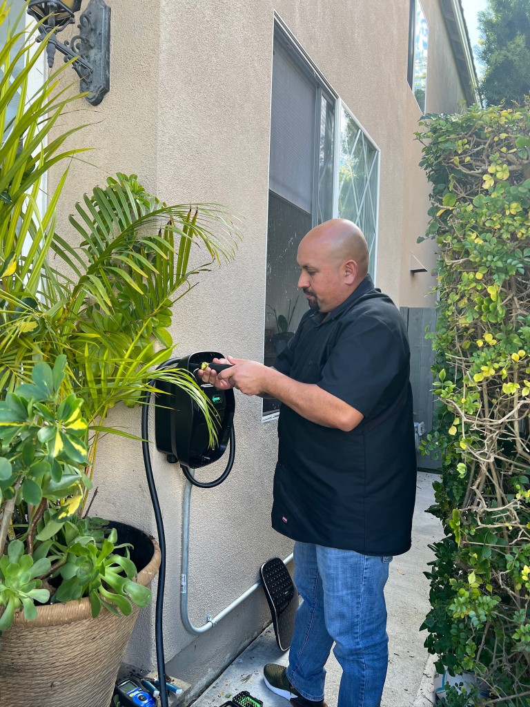 evNation technician testing a wall-mounted EV charger on a home exterior
