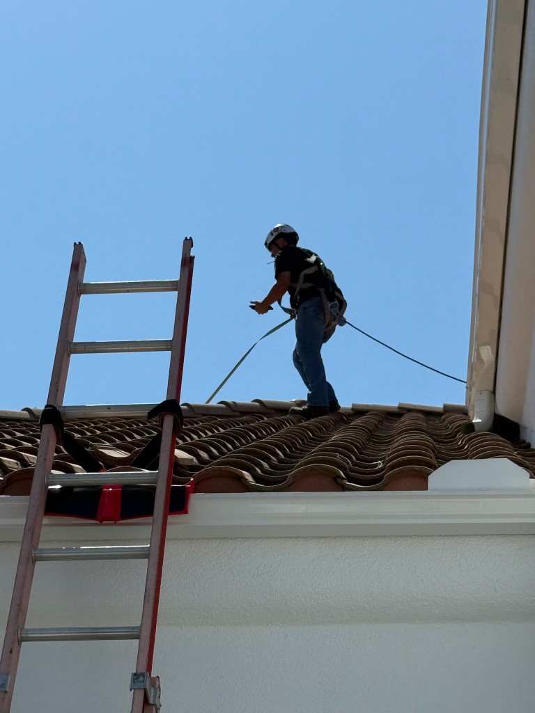 Technician on a residential roof wearing a safety harness and hard hat